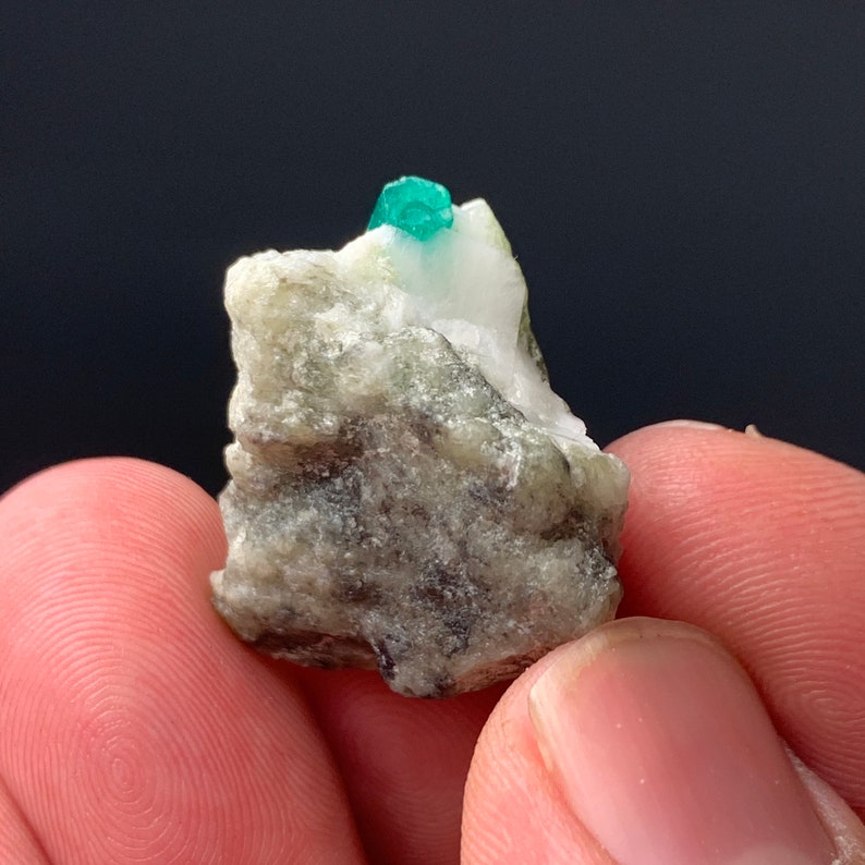 Puede incluir: Un peque&ntilde;o cristal de esmeralda verde incrustado en una matriz de roca gris y blanca.