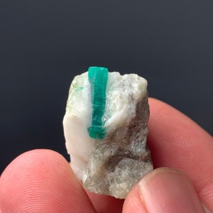 Puede incluir: Un peque&ntilde;o cristal de esmeralda verde incrustado en una matriz de roca blanca y gris. El cristal mide aproximadamente 2,5 cm de largo y tiene una punta afilada.