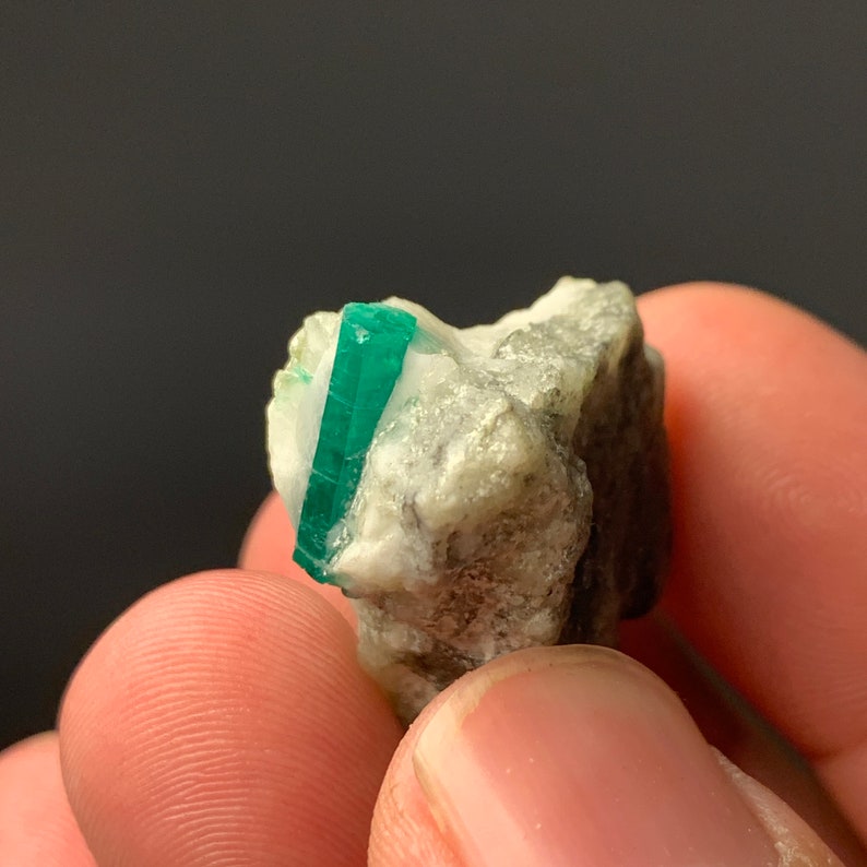 Puede incluir: Un peque&ntilde;o cristal de esmeralda verde incrustado en una matriz de roca blanca, gris y marr&oacute;n.