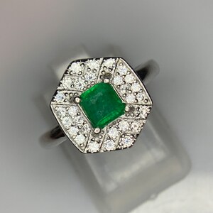 May include: A silver ring with a square emerald gemstone surrounded by smaller diamonds.