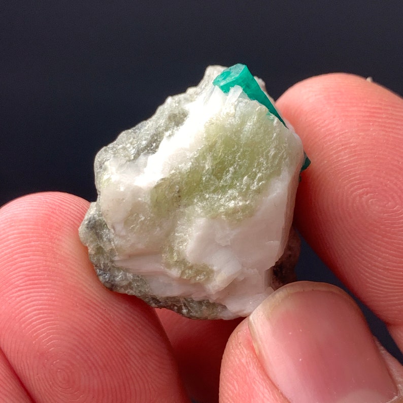 Puede incluir: Un peque&ntilde;o cristal de esmeralda verde incrustado en una matriz de roca blanca y gris.