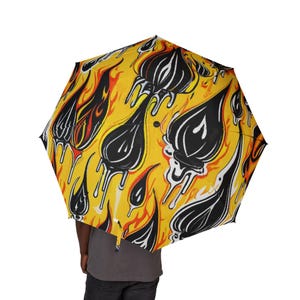 May include: A yellow umbrella with a repeating pattern of black and white teardrop shapes with dripping white accents, set against a background of orange flames. The umbrella is open, and the handle is not visible.