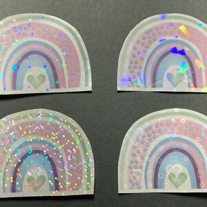 May include: Four iridescent rainbow stickers with a heart in the center. Each sticker has a different holographic pattern, including stars, confetti, and dots.