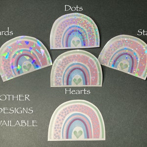 May include: Five rainbow stickers with different holographic designs: dots, shards, stars, hearts, and a design with small circles. Each sticker features a rainbow with a small heart in the center.
