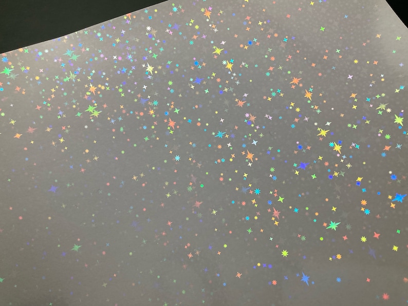 May include: A sheet of iridescent holographic paper with a scattered pattern of small stars in various colors, including blue, green, yellow, and pink.