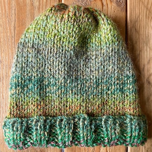Peut inclure: Un bonnet tricoté à la main dans des tons de vert, jaune et marron. Le bonnet présente un bord côtelé et un motif tricoté texturé. Les couleurs se fondent, créant un aspect naturel et terreux. Ce chapeau chaud est idéal pour le froid.