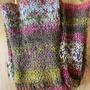 Könnte beinhalten: Ein handgestrickter Schal in verschiedenen Farben, darunter Rosa, Grün, Braun und Weiß. Der Schal ist aus dickem Garn gefertigt und hat ein strukturiertes Aussehen. Das Farbmuster ist gestreift, wobei die Farben ineinander übergehen. Der Schal ist gefaltet.