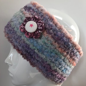 May include: A multi-coloured crocheted headband with a pink and brown flower accent. The flower has a white button with a pink star in the centre.