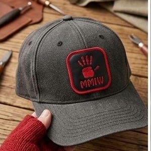 May include: A charcoal gray baseball cap featuring a square black patch with a red embroidered handprint and the text MMIW in red. The cap has a structured crown, a curved brim, and stitched eyelets on the top panels for ventilation and durability.