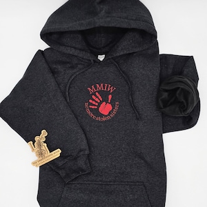 May include: A dark gray hooded sweatshirt with a red handprint and the text "MMIW no more stolen sisters" on the front.