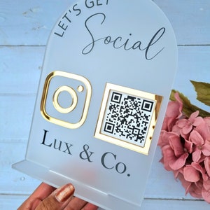 May include: White acrylic sign with the text "Let's Get Social" in black. The sign features a gold Instagram logo and a gold framed QR code. The text "Lux & Co." is printed below the logos.