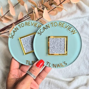 May include: Two light blue round coasters with gold lettering. The coasters say "Scan to Review" and "TL Nails". Each coaster has a square window with a glittery design.
