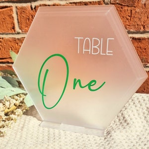 May include: A frosted hexagonal table number sign with a green cursive "One" and the word "TABLE" in white text.