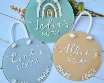May include: Three round, acrylic door signs with white lettering and decorative elements. The signs are in light blue, gray, and beige. The signs read "India's Room", "Esme's Room", and "Albie's Room".