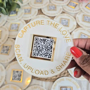 May include: Circular white and gold coasters featuring a QR code and the text "CAPTURE THE LOVE, SCAN, UPLOAD & SHARE". The text is in gold. Several coasters are visible.
