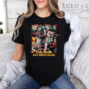 May include: Black t-shirt with a collage of images of a man playing guitar with the text "Tyler Hilton AKA Chris Keller" and song titles like "When You Right My Name", "First Noticed", "Taking My Heels", "Holding You", "You Had To Go", "Friends Of Mine", "Something Beautiful", "That Lady" and "I Know What You Did Last Summer".
