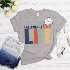 K&ouml;nnte beinhalten: Graues T-Shirt mit einer Grafik im Vintage-Stil, auf der "Livin' that Volleyball Mom Life" steht, mit einer Volleyball-Grafik &uuml;ber dem Text.