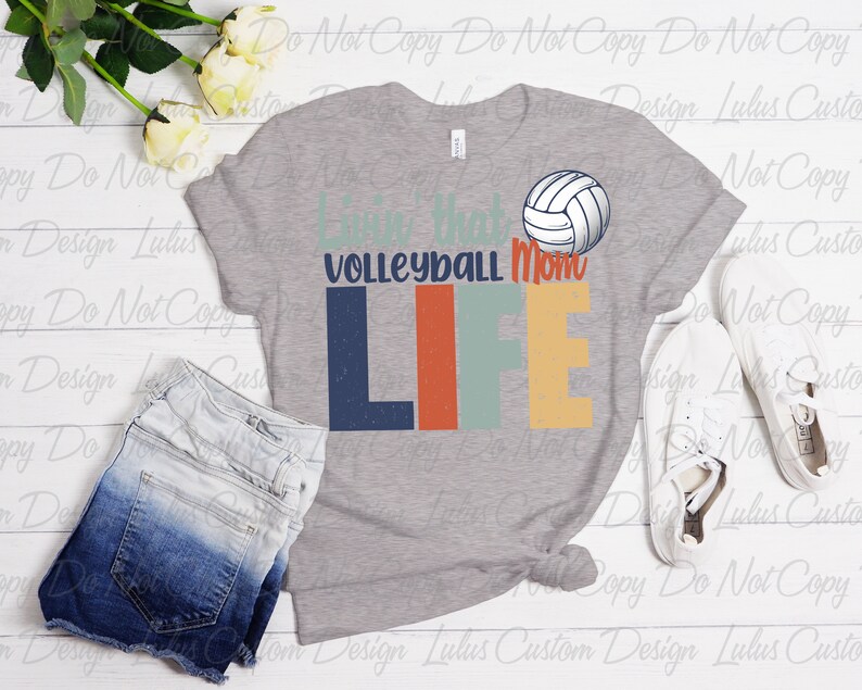 K&ouml;nnte beinhalten: Graues T-Shirt mit einer Grafik im Vintage-Stil, auf der "Livin' that Volleyball Mom Life" steht, mit einer Volleyball-Grafik &uuml;ber dem Text.