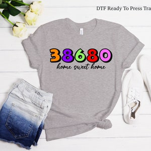 May include: A gray t-shirt with a colorful design of the numbers 38680 and the text "home sweet home".