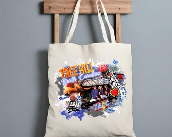 May include: Cream-colored tote bag featuring a collage design with the words "Tree Hill North Carolina" in orange and blue. The design includes images of a bridge, a car, and a group of people. The bag has two cream-colored handles.