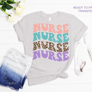 May include: A gray t-shirt with a ready-to-press transfer design that says "NURSE" four times in a retro font. The word "NURSE" is in different colors, including pink, teal, brown with a leopard print, and purple.