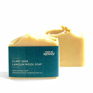 May include: Two bars of Clary Sage Lanolin Wool Soap. The soap has a light beige color with a textured top. One bar has a teal label with white text that reads "Clary Sage Lanolin Wool Soap" and "100% Natural Soap". The brand name "west of kerry" is also visible.