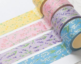 Könnte beinhalten: Vier Rollen Washi-Tape mit Blumenmustern und goldenen Akzenten. Die Bänder zeigen gelbe Blumen, rosa Blumen, lila Lavendel und weiße Blumen auf blauem Hintergrund.