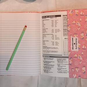 May include: Open notebook with lined pages and a green pencil with a red eraser. The notebook cover is pink with a nautical-themed pattern. The notebook includes metric unit conversions and punctuation information. The text "Handmade for you by Spenwick Cottage Designs" is visible.