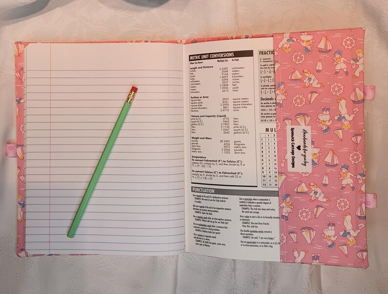 May include: Open notebook with lined pages and a green pencil with a red eraser. The notebook cover is pink with a nautical-themed pattern. The notebook includes metric unit conversions and punctuation information. The text "Handmade for you by Spenwick Cottage Designs" is visible.