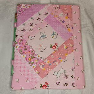 May include: A pink and white quilted notebook cover with a variety of patterns. The cover features floral, polka dot, and nautical-themed fabric patches. The design includes images of kittens, sailboats, and a white dog.