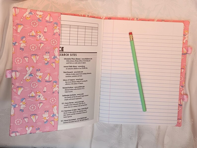May include: Open notebook with lined pages and a green pencil. The cover is pink with a nautical pattern of sailors, sailboats, and anchors. The left page has a list of search sites.