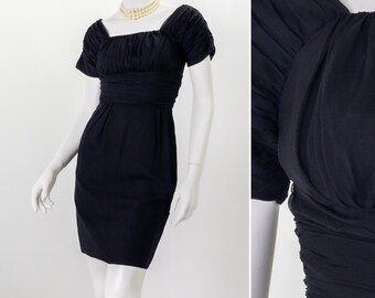 May include: A black short-sleeved dress with a square neckline and a fitted silhouette. The dress has a gathered detail at the shoulders and a cinched waist.