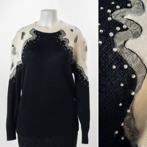May include: Black sweater with white fuzzy trim and pearl embellishments. The sweater has a round neckline and long sleeves.