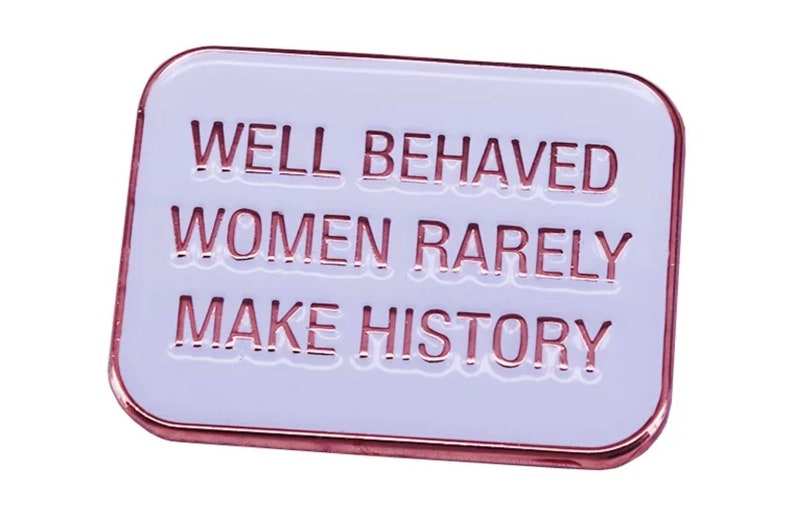 May include: White enamel pin with a rose gold border. The pin features the text "WELL BEHAVED WOMEN RARELY MAKE HISTORY".