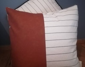May include: Two decorative throw pillows, one with a brown leather-like fabric and the other with white fabric with black stripes.