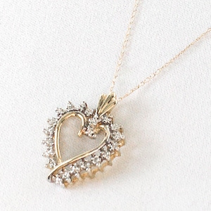 May include: A gold-toned heart pendant necklace with a delicate chain. The heart is outlined with gold and encrusted with small, sparkling stones. The necklace is displayed on a white background, highlighting the jewelry's design.