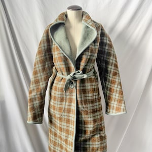 May include: A vintage plaid coat in brown, blue, and green, displayed on a mannequin. The coat features a shawl collar, a matching belt, and a light green lining. The coat has two pockets and is knee-length.