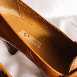 May include: Close-up of a pair of brown leather high heels. The interior of the shoe is a light tan colour, with a label that reads "Gucci Made in Italy." The heel is a dark brown colour.