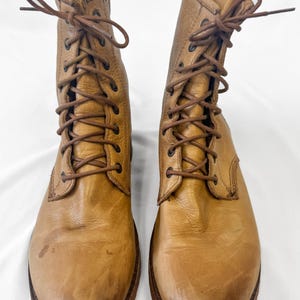 May include: A pair of tan leather lace-up boots. The boots have a worn appearance with visible creases and scuffs. The soles are dark brown, and the laces are a matching brown color. The boots are displayed against a white background.