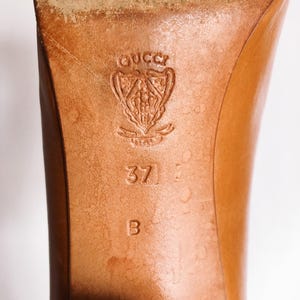May include: Close-up of a brown leather shoe sole. The Gucci logo is embossed near the heel, with size 37 and the letter B. The leather shows signs of wear.