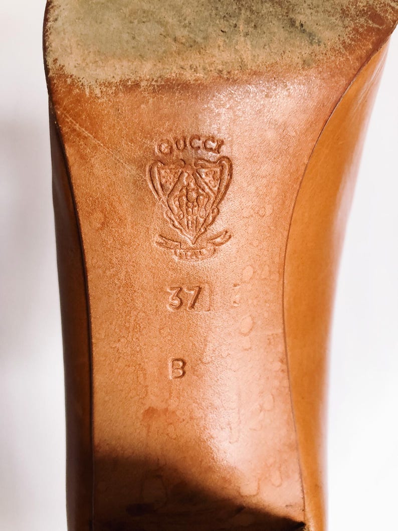 May include: Close-up of a brown leather shoe sole. The Gucci logo is embossed near the heel, with size 37 and the letter B. The leather shows signs of wear.