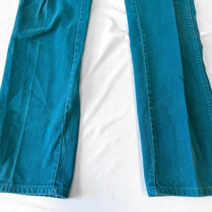 May include: A pair of teal-colored pants featuring a straight-leg cut and a classic denim-style construction with visible vertical seams along the legs. The fabric has a consistent solid teal hue throughout, with a standard hem at the bottom.