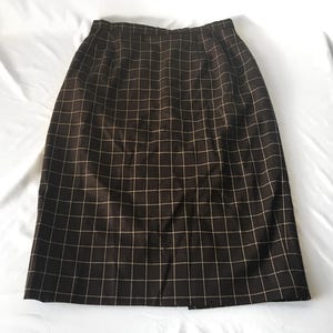 May include: A brown knee-length skirt with a grid pattern of thin, light beige lines. The skirt has a straight cut and a slit at the back hem. The fabric appears to be a woven material.