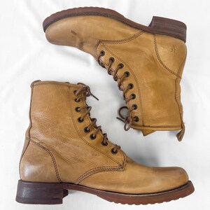 May include: A pair of tan leather lace-up boots. The boots have a worn appearance with visible creases and scuffs. The soles and heels are a darker brown. The boots are displayed on a white background.