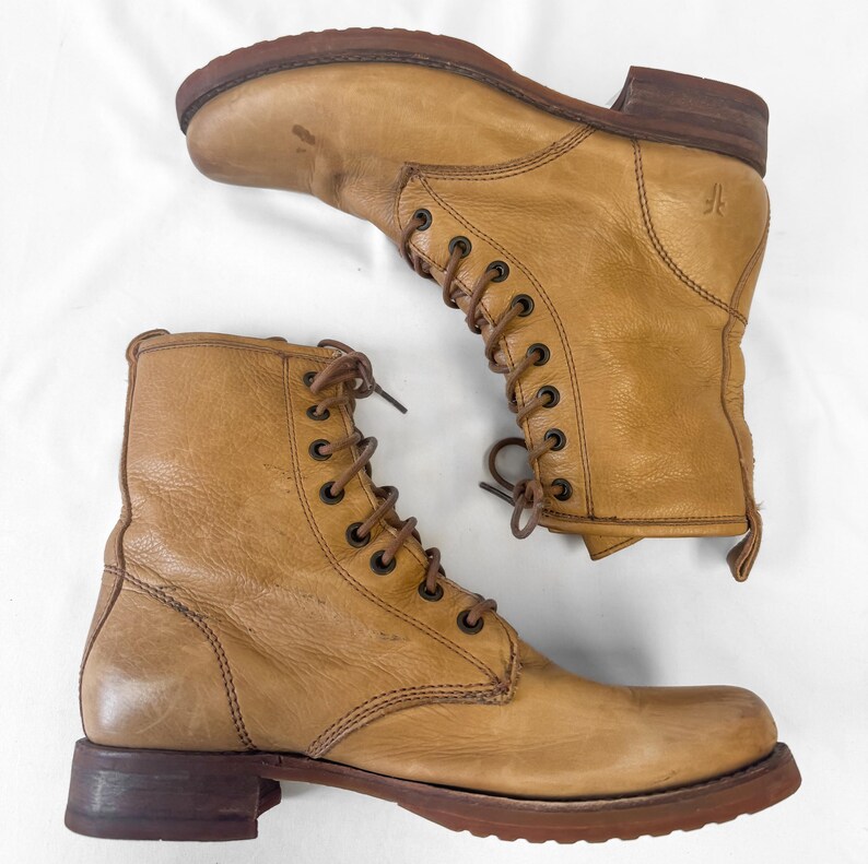 May include: A pair of tan leather lace-up boots. The boots have a worn appearance with visible creases and scuffs. The soles and heels are a darker brown. The boots are displayed on a white background.