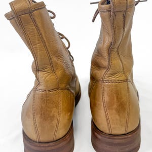 May include: A pair of tan leather boots with laces. The boots have a worn appearance, with visible creases and a slightly distressed finish. The soles are a darker brown, and the boots appear to be well-constructed.