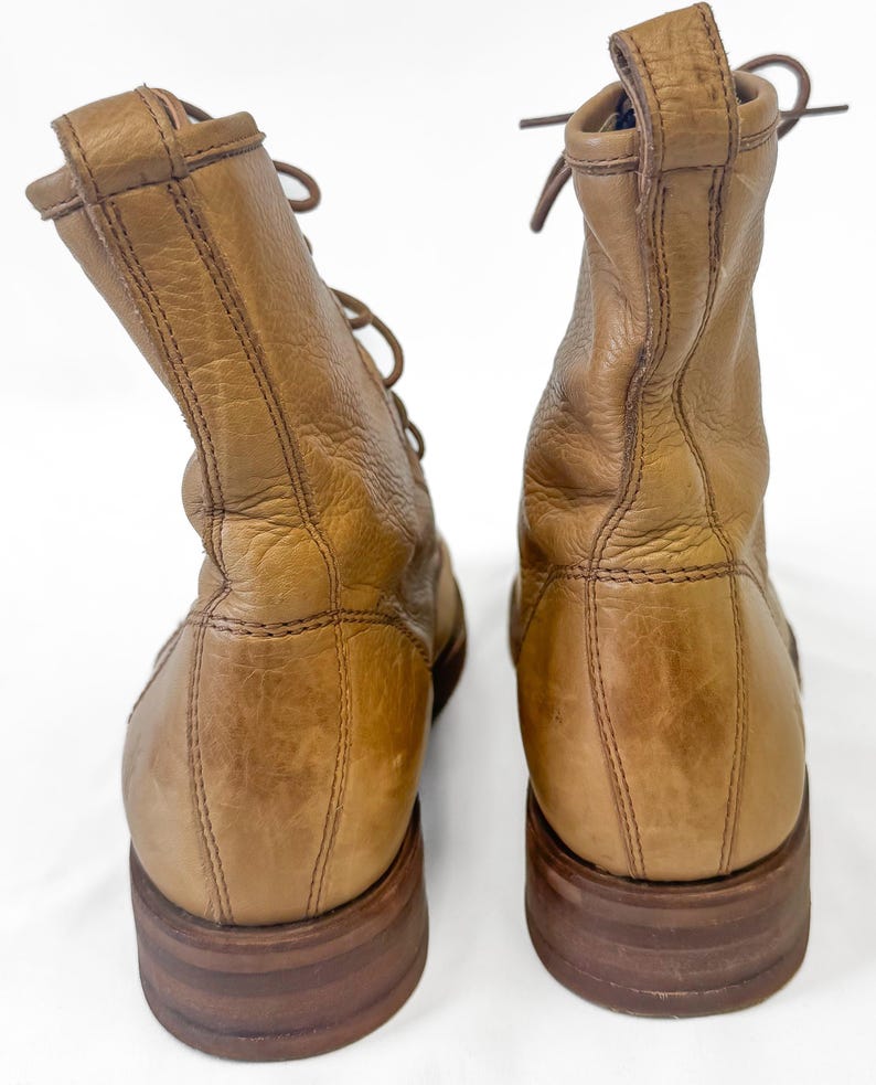 May include: A pair of tan leather boots with laces. The boots have a worn appearance, with visible creases and a slightly distressed finish. The soles are a darker brown, and the boots appear to be well-constructed.