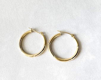 May include: A pair of gold hoop earrings. Each earring has a circular design with a hinged post closure. The earrings are made of a shiny gold material and are displayed on a white surface.