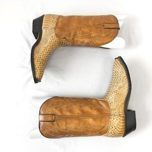 May include: A pair of cowboy boots with a tan leather upper and a snakeskin-textured vamp. The boots have a pointed toe, a stacked heel, and decorative stitching. The boots are set against a white background.