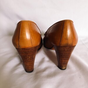 May include: A pair of vintage brown leather heels with wooden cone-shaped heels. The shoes have a classic design with a rounded toe and a small decorative detail on the vamp. The heels appear to be approximately 7.6 cm tall.